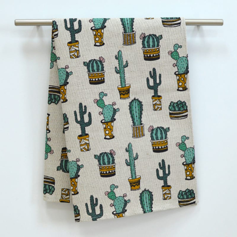 Cream textile with green and gold cactus and potted plant pattern, hanging from metal rod against white wall