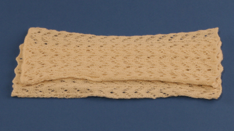 Woven natural fiber headband or textile strip with geometric dot pattern, displayed flat against blue background
