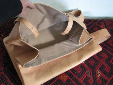 Beige canvas tote bag with rope handles, displayed open on a red patterned textile, showing interior lining detail