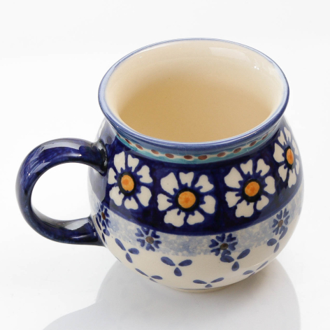 Navy ceramic mug with white and yellow floral pattern, filled with light tea, rounded shape with handle