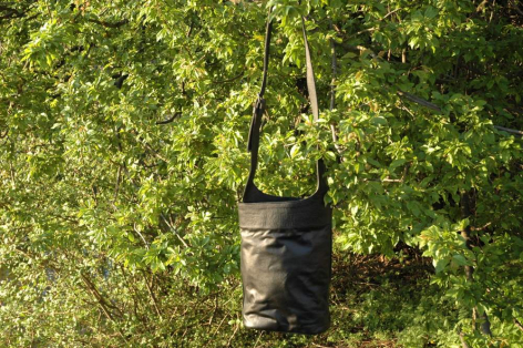 Rolled dark textile hanging from rope against vibrant green leafy background, overhead view