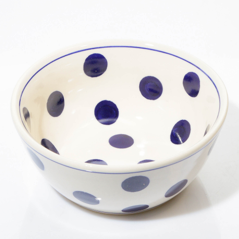 Cream ceramic bowl with hand-painted dark blue polka dots, viewed from above at a slight angle