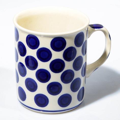 Cream ceramic mug with repeating navy blue polka dot pattern and curved handle, front three-quarter view