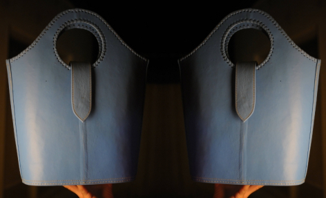 Pair of slate blue leather bags with rounded tops and circular handles, front view showing vertical slit detail