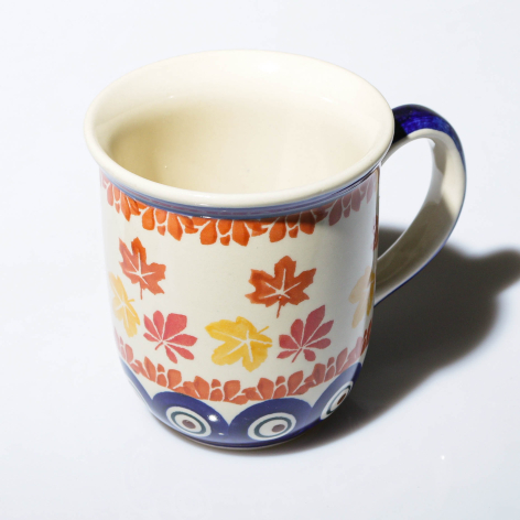 Ceramic mug with cream interior and blue handle, decorated with red and yellow floral pattern on white base, front view