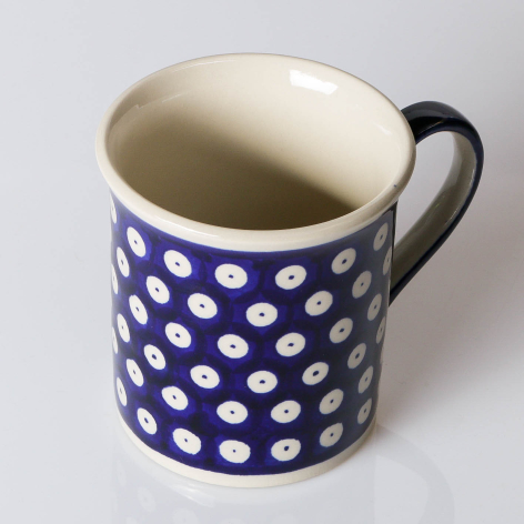Navy ceramic mug with white polka dot pattern and black handle, cream interior, shown from front angle