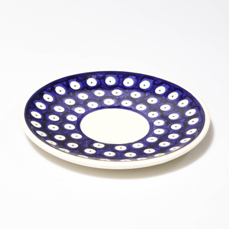 Deep blue ceramic plate with white polka dot pattern and cream-colored rim, angled three-quarter view