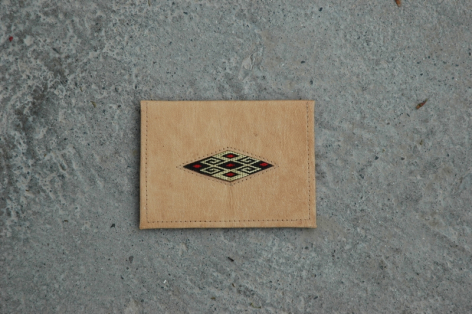 Étiquette artisanale en cuir beige clair avec motif géométrique noir gravé, vue de face sur surface grise