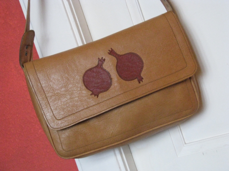 Tan leather shoulder bag with burgundy embroidered leaf design on front flap against striped background