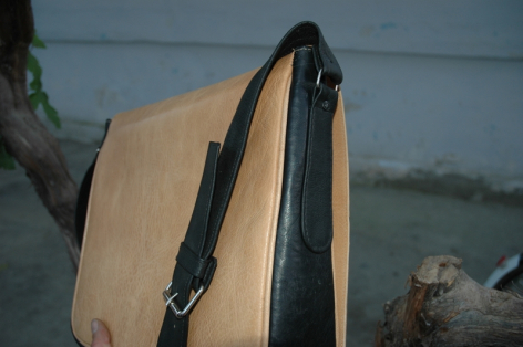 Beige canvas backpack with black leather straps and trim, shown from front angle against grey background
