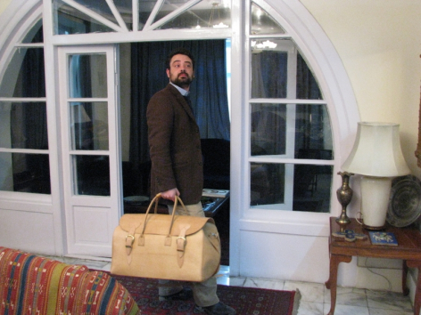 Woman in dark coat holding tan leather handbag, standing in doorway with white arched doors behind her