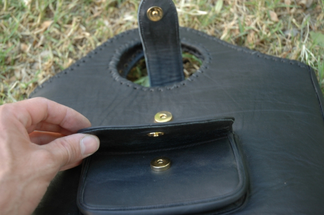 Hand holding open black leather pouch with brass snap closure, interior view showing card slot detail