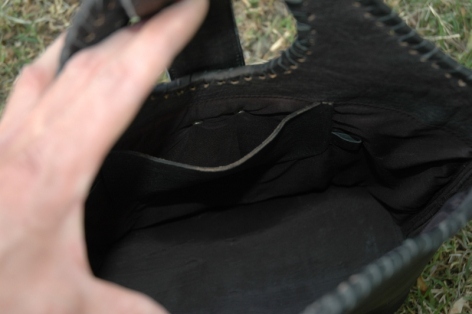 Hand opening dark leather bag to reveal black fabric interior lining