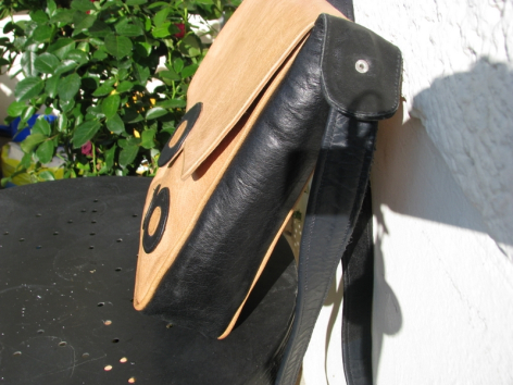 Black leather shoulder bag with tan suede panel, shown open to display interior compartment and black strap