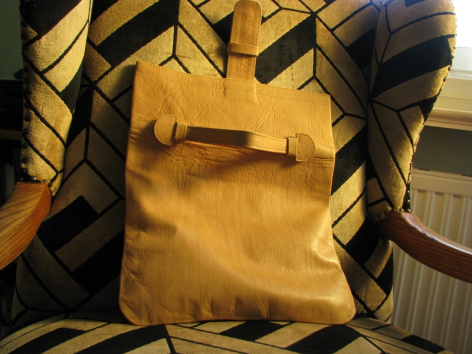 Mustard yellow leather crossbody bag with front pocket detail, displayed on patterned textile background