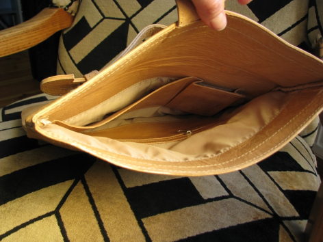 Tan leather pouch with open top revealing interior, displayed flat on geometric patterned surface