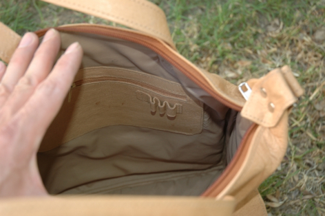 Tan leather bag held open showing olive green interior lining and craftsmanship detail