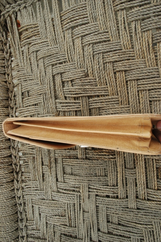 Natural wooden weaving shuttle with brass fittings resting on woven textile with geometric pattern