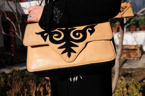 Tan leather clutch bag with black decorative bird motif on front flap, displayed open against dark background