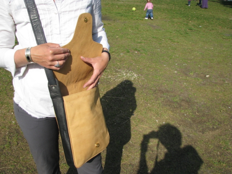 Tan leather bag held open by hands showing interior compartments and craftsmanship detail