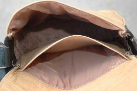 Tan leather bag open from above, showing soft grey lining and interior compartment with metal clasp detail