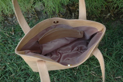 Tan leather tote bag with open top showing brown fabric lining, viewed from above on grass