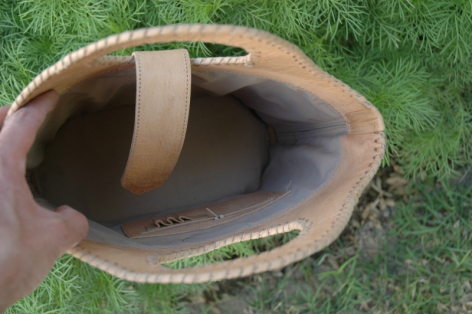 Brown leather bowl with tan handle, viewed from above on green grass background