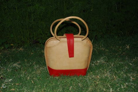 Cream and terracotta leather bag with curved wooden handles, front view against green textured background
