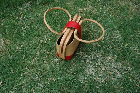 Handcrafted wooden toy with red center and two circular brass rings, viewed from above on green textured background