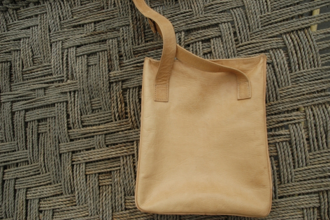 Tan leather shoulder bag with wooden handle, front view on patterned textile background
