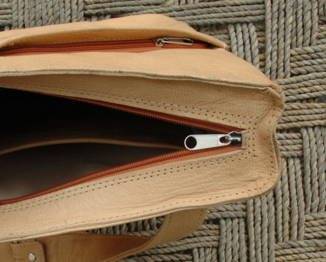 Tan leather bag open to show interior compartment with small metal clasp detail, viewed from above