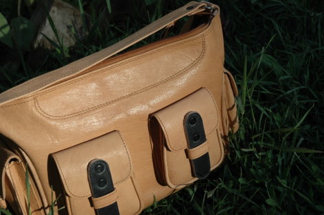 Tan leather waist bag with black buckle details, front view showing rounded shape and structured compartments