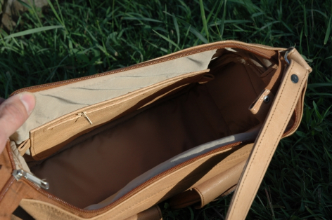 Tan leather bag open flat, showing dark brown interior, photographed from above on grass
