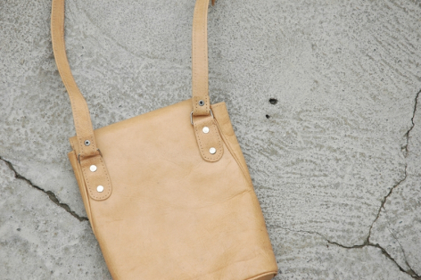 Tan leather crossbody bag with natural handles, front view on concrete surface
