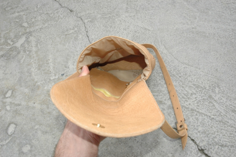 Tan leather drawstring pouch held open in hand, showing interior and gathered rope closure from above