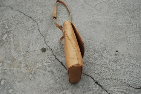 Wooden shoehorn with curved handle and natural tan finish, displayed flat against concrete surface