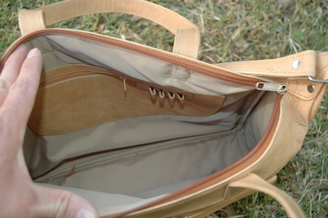 Tan leather bag held open showing interior canvas lining and structured compartment, front view