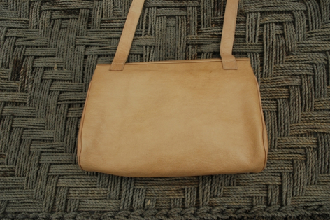 Tan leather shoulder bag with dual handles, displayed flat on woven background, front view