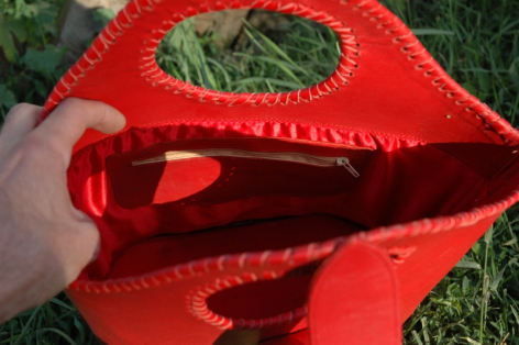 Bright red leather bag with curved lip-shaped opening and red handles, front view detail