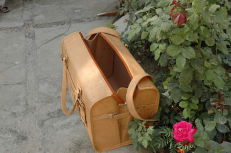 Tan leather tote bag with rolled handles and circular wooden base detail, front view on stone surface with pink flowers