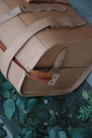 Tan leather bag with brown straps, overhead view showing rolled construction and natural material texture