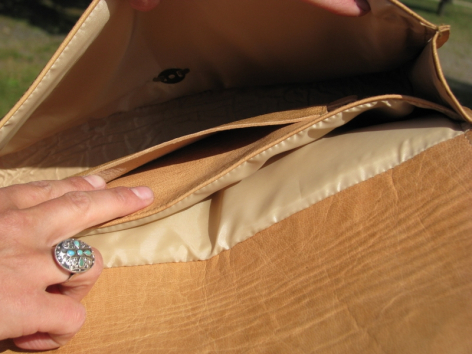 Tan leather bag open to reveal cream linen interior with decorative beaded clasp detail, viewed from above