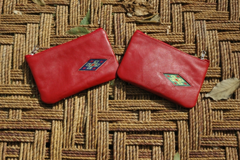 Two red leather wallets displayed open on a woven natural fiber mat, showing interior card slots and coin pouches