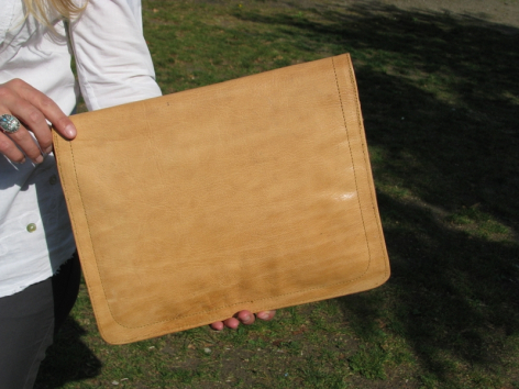 Tan leather clutch held in hands, front view showing smooth finish and rectangular shape