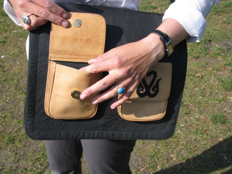 Sac à bandoulière en cuir noir et beige, porté à l'épaule, vue de face montrant la poche frontale distinctive