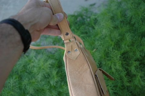 Main en train de coudre du cuir beige à la main avec du fil, détail du travail artisanal sur tissu vert
