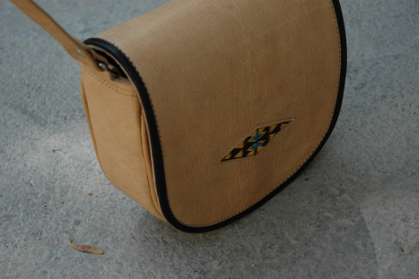 Sac en cuir beige avec détail de couture noire, vue de trois quarts sur surface grise