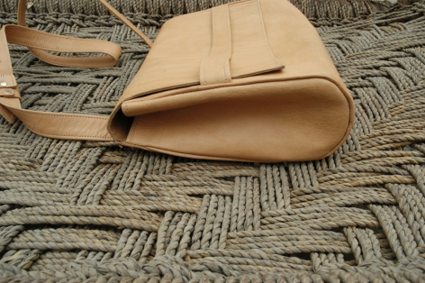 Sac à main en cuir beige clair, forme trapézoïdale, vue de dessus avec anses visibles sur fond textile géométrique
