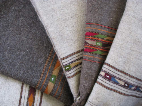 Folded textiles in neutral tones with striped borders in red, gold, and burgundy displayed in close-up detail