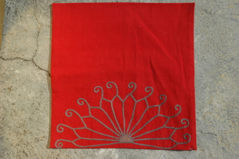 Tissu rouge carré avec motif géométrique brodé gris en éventail, vue de dessus